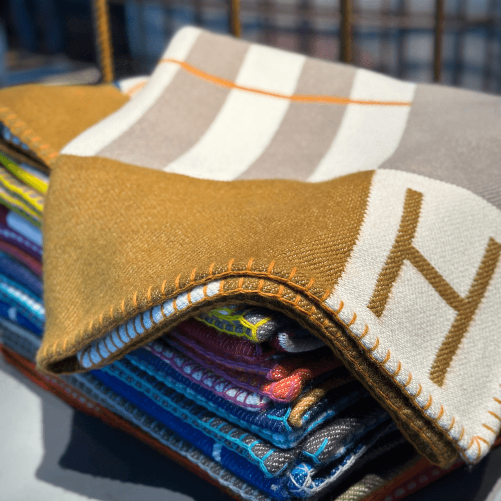 Hermès Home — folded wool blankets in mustard and stripe, the H monogram in gold, a study in material restraint