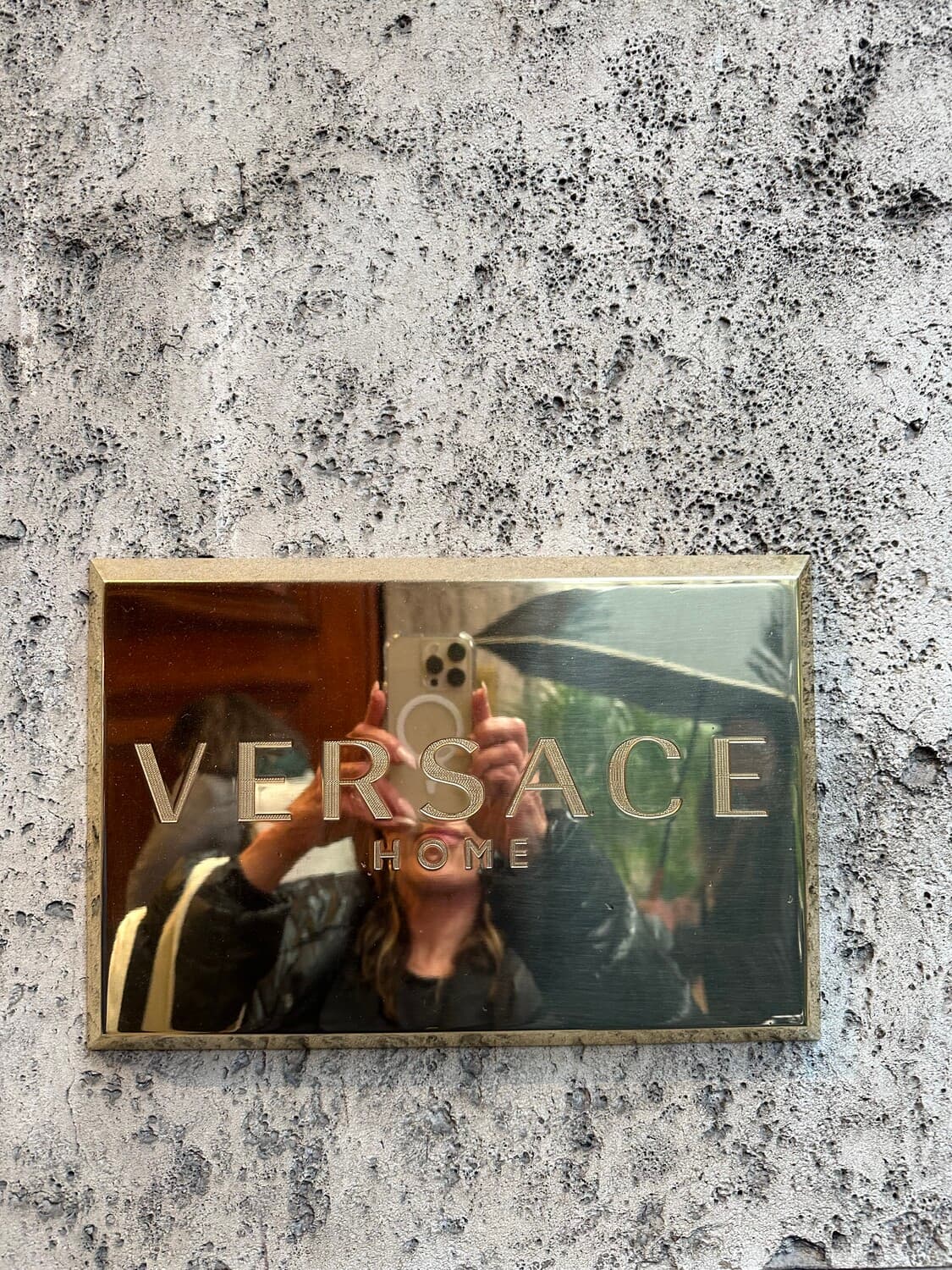 Versace Home — a golden plaque on aged stone, the reflection of Milan in the glass