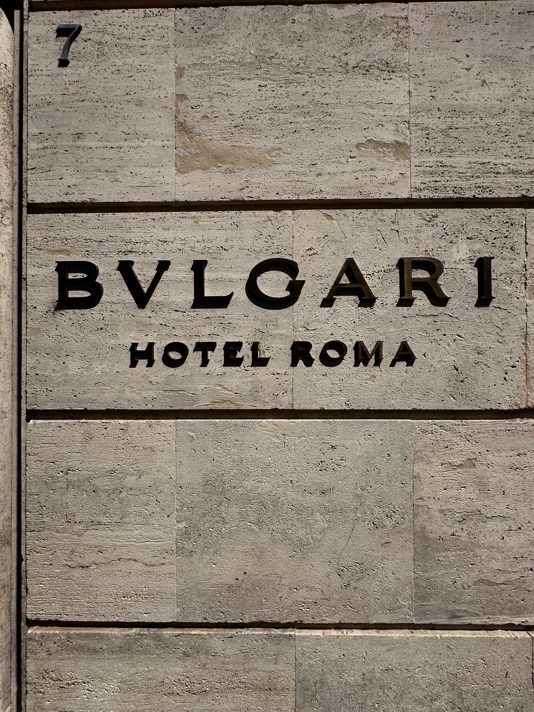 Travertine facade with bronze lettering reading Bulgari Hotel Roma.