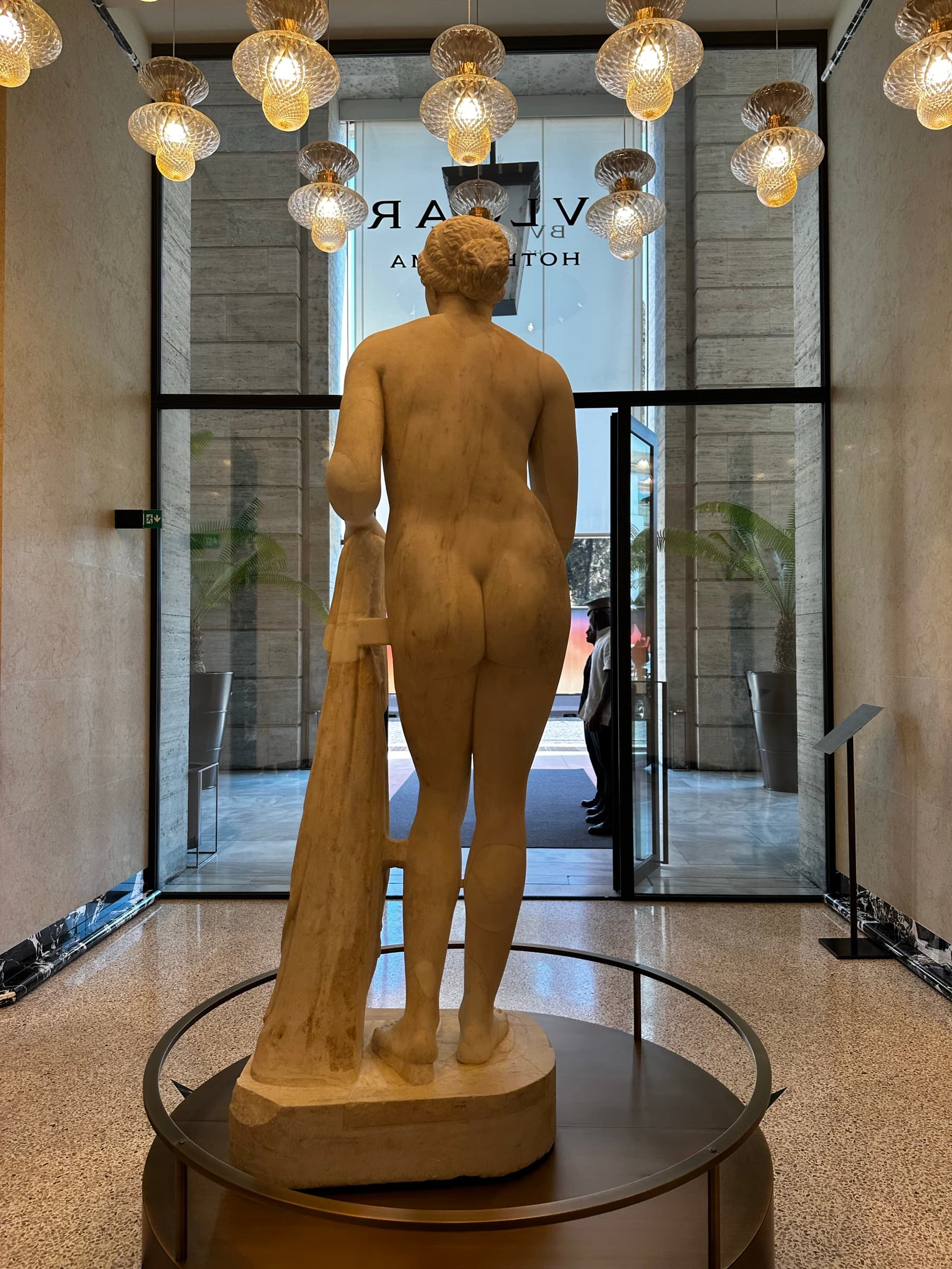 The same figure seen from behind, looking out through the glass entrance of the hotel.