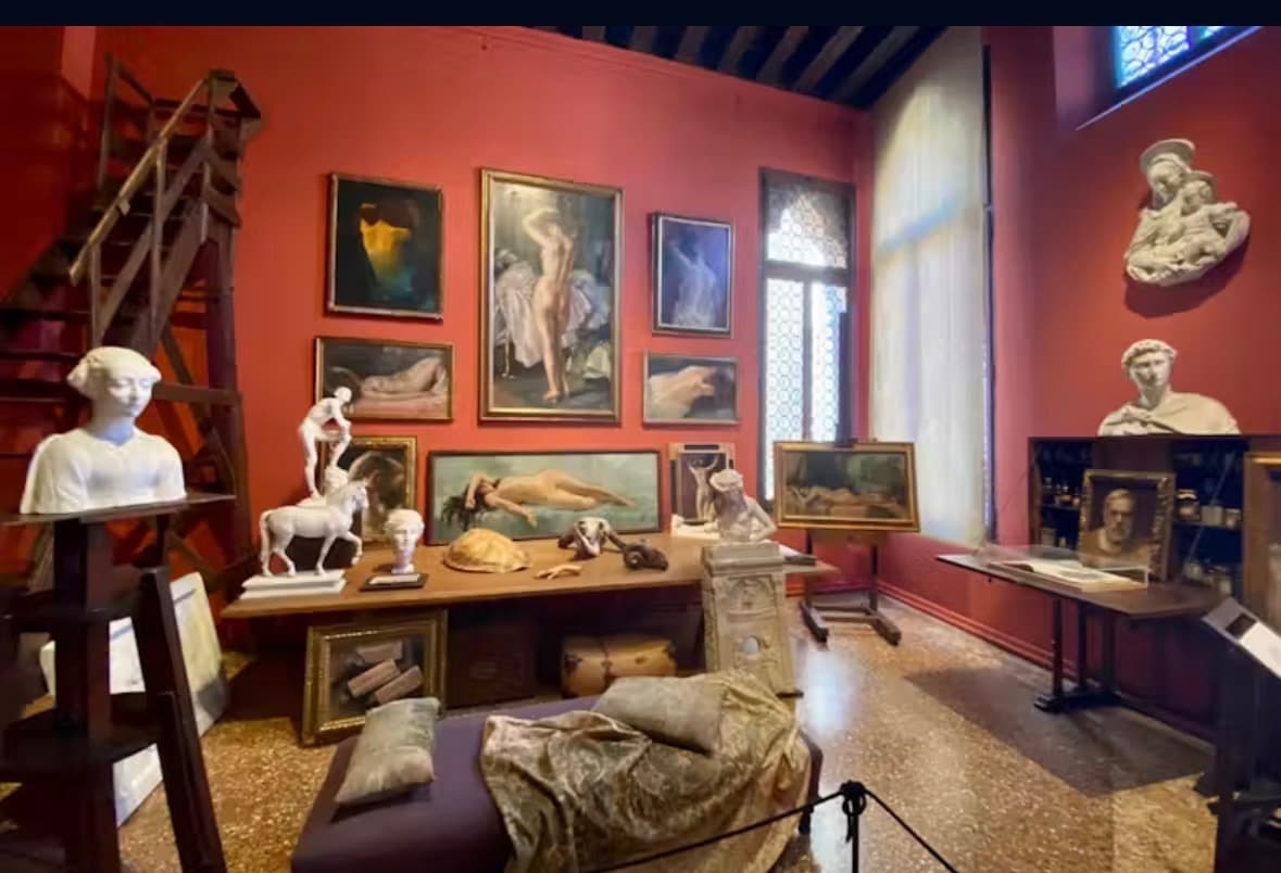 Interior room at Palazzo Fortuny with terracotta walls, oil paintings, and marble sculptures.