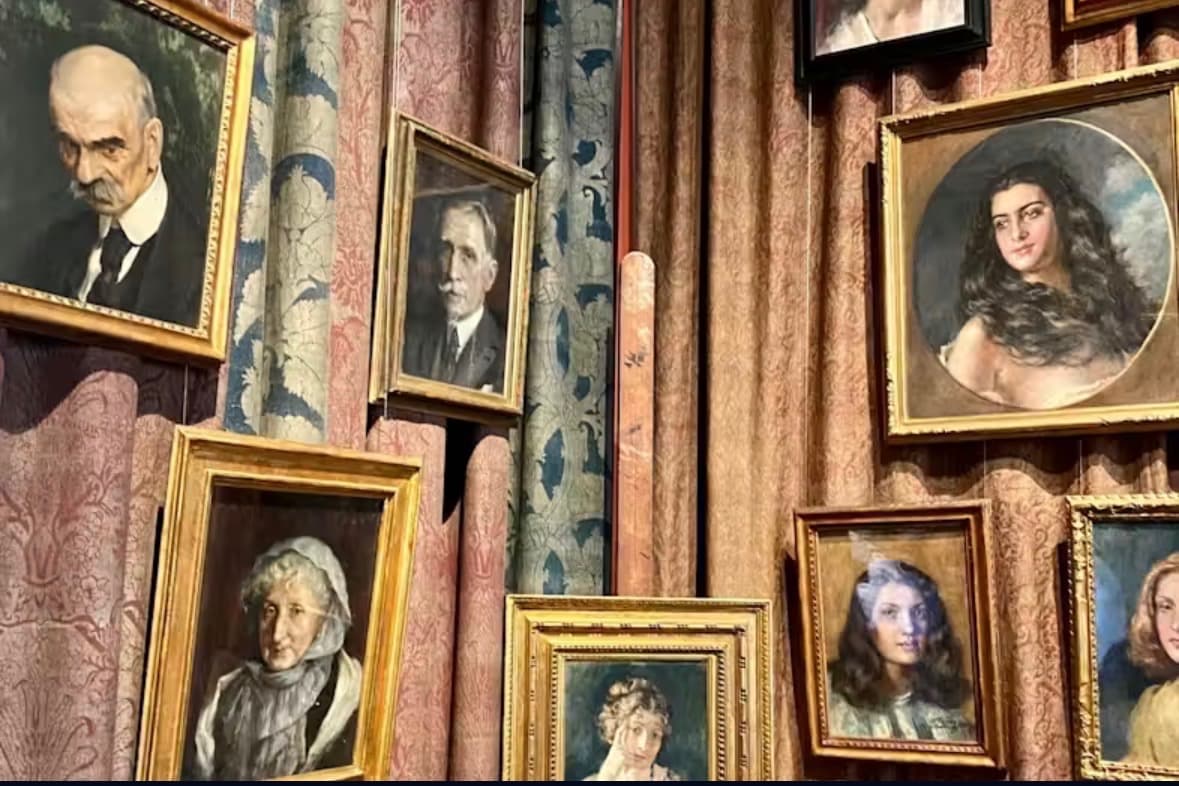 Gilt-framed portrait paintings hung over layered rose and blue Fortuny damask fabric at Palazzo Fortuny.