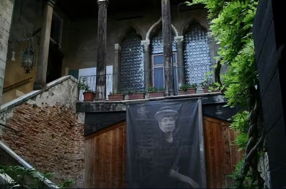 Exterior courtyard of Palazzo Fortuny, Venice — Gothic arched windows and a banner portrait hung over an ancient brick wall.