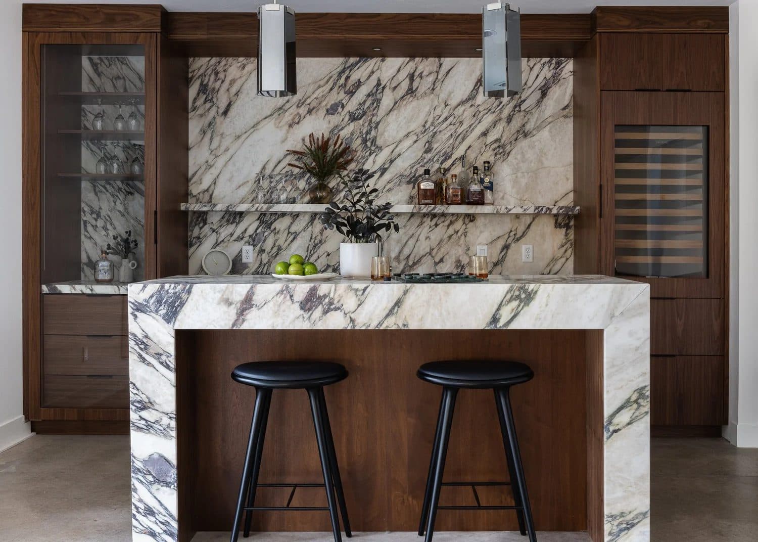 Dark walnut kitchen with dramatic veined marble island, two black barstools, and pendant lights above.