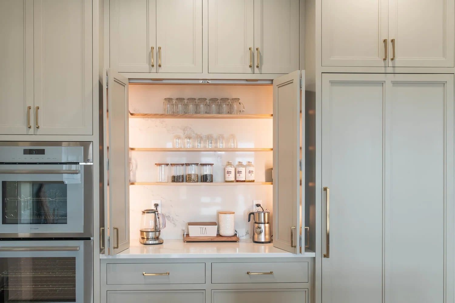 White kitchen with open butler's pantry cabinet, lit interior shelves holding glassware and small appliances.