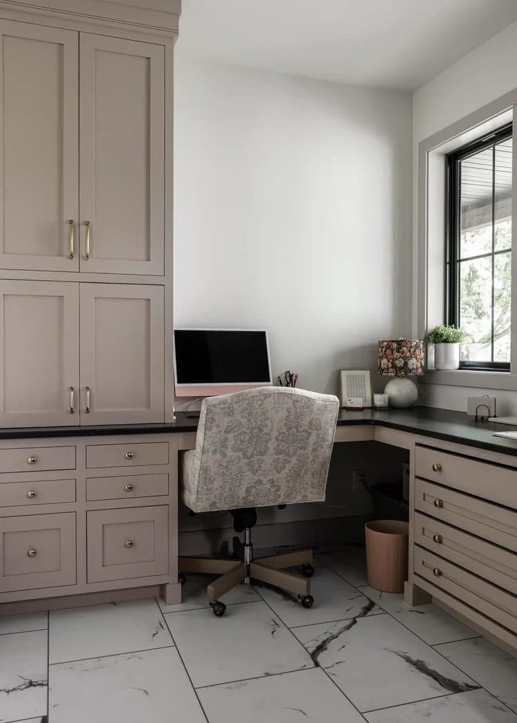 Built-in home office desk and cabinetry in greige with black countertop and corner window.