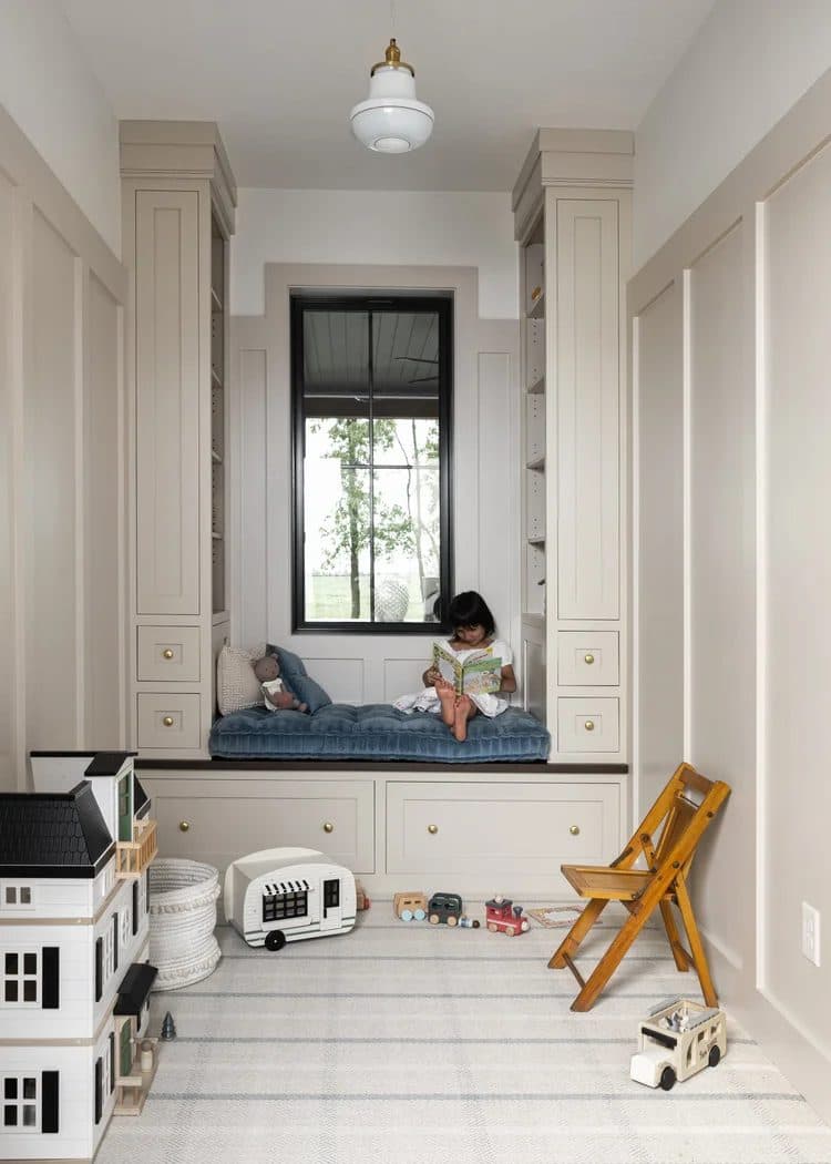 Children's built-in window seat flanked by cream cabinetry, with a child sitting in the nook.