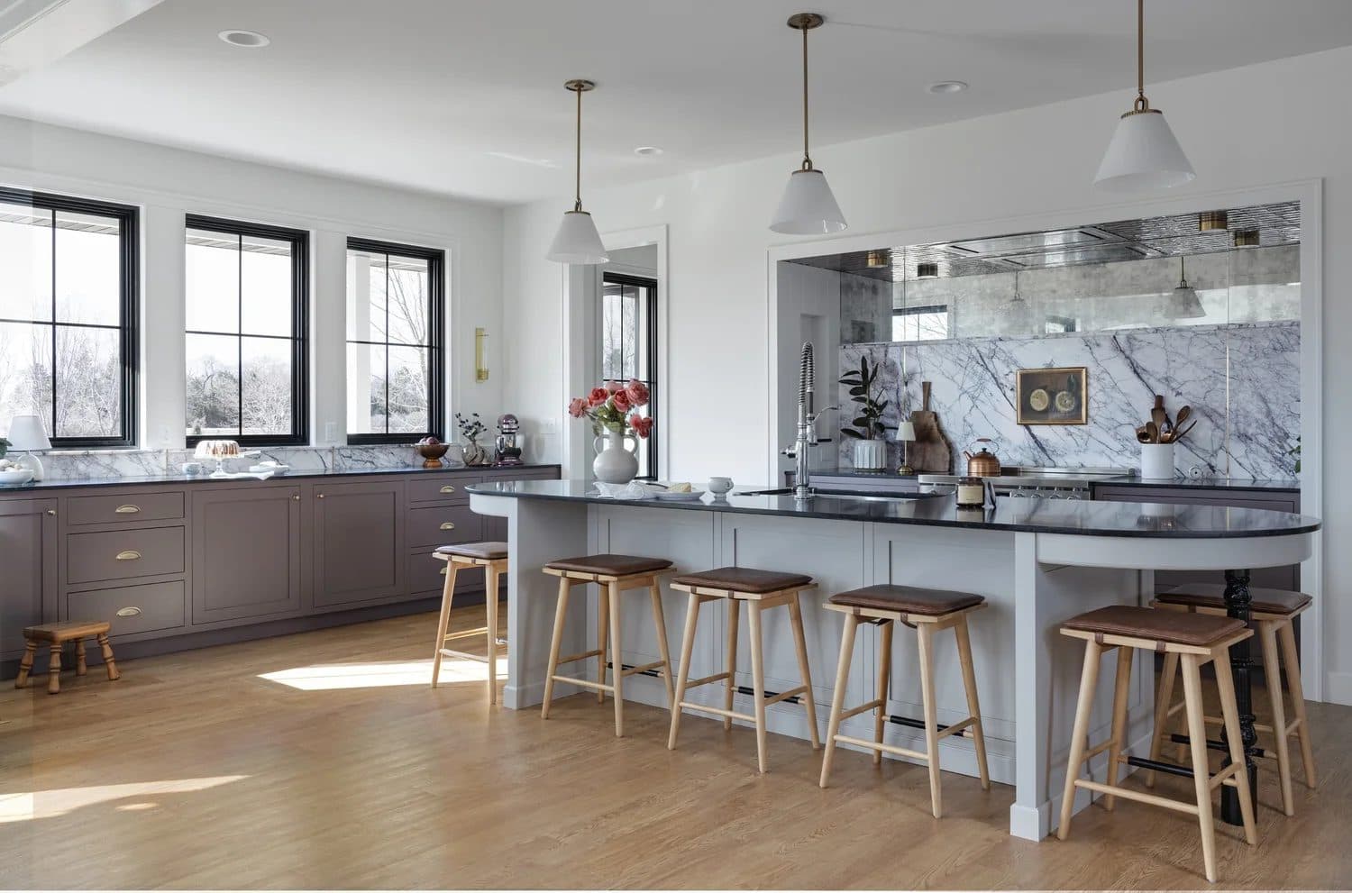 Gray kitchen with long marble island, five barstools, pendant lights, and large windows.