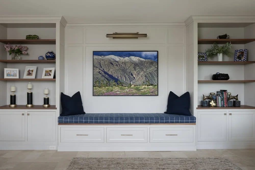 White living room built-in window seat and shelving with a landscape painting and blue ticking cushion.