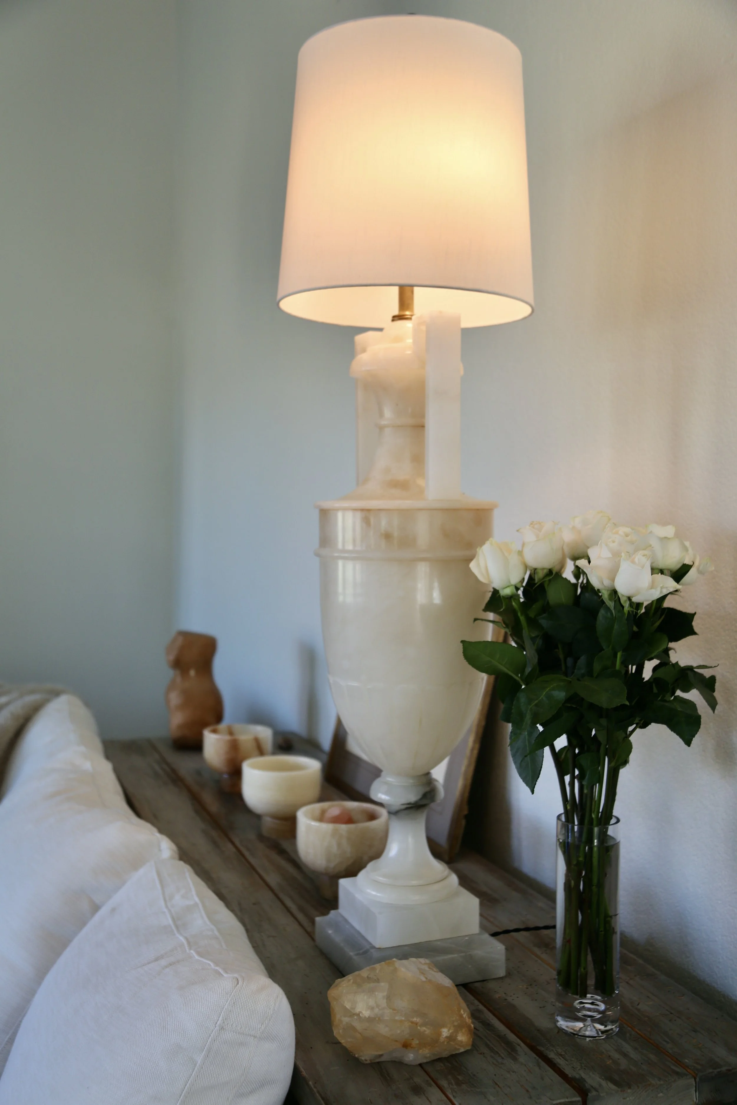 Tall lamp, vase of white roses, and decorative bowls on a wooden table